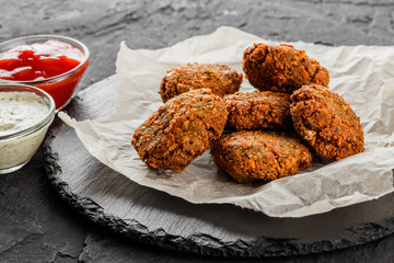 Roasted chickpeas falafel patties with garlic yogurt sauce and tomato sauce on paper over dark stone background. Healthy vegan food, clean eating, dieting, close up