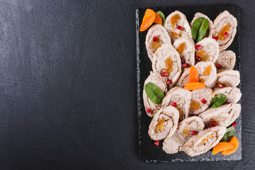 Assorted meat, stuffed chicken roll, meat roll with pomegranate, greens on black shale background. Meat appetizer, food concept. Top view.