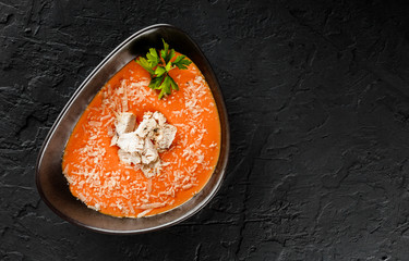 Carrot cream soup with chicken fillet and parmesan cheese in bowl on black stone background. Healthy food, top view.