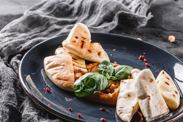 Chickpeas hummus with olive oil, paprika, pine nuts and pita bread in a ceramic plate over grey...
