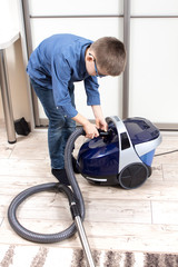 Sprzątanie mieszkania. Obowiązki domowe dzieci. Chłopiec przygotowuje odkurzacz do sprzątania...