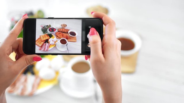 Female hand taking photo of appetizing breakfast on table using smartphone POV shot