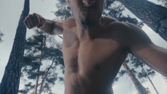 Aggressive shirtless man brutally beats lying opponent outdoor at forest.