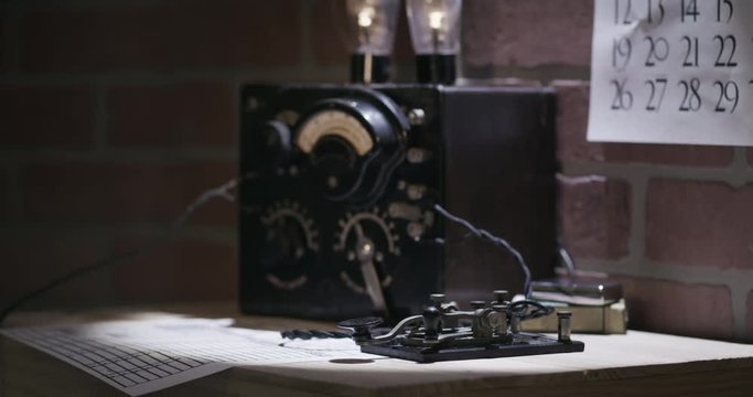 A spy time in the WWII era picks up headphones and commences to transmit messages in Morse Code using a code key.