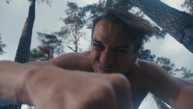 Crazy aggressive shirtless man beats with his fists the lying person outdoor at forest