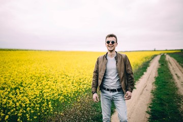 man wearing round steampunk sunglasses and a brown leather jacket in a summer yellow flowered field