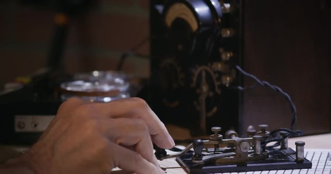 A cold war era spy sending messages via Morse Code using a code key with tape recorder going in the background.