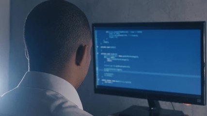 Back view of programmer professional programming code on computer monitor at night office