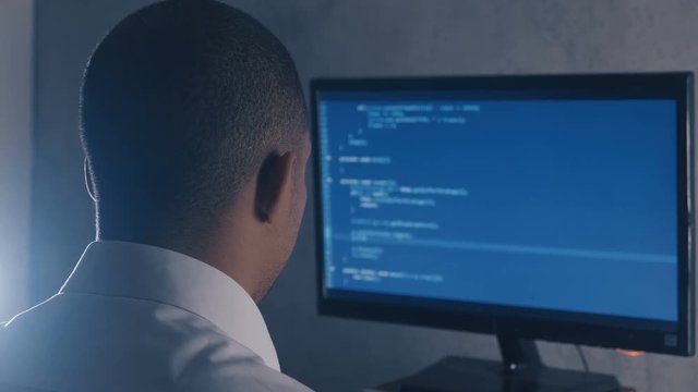 Back view of programmer professional programming code on computer monitor at night office