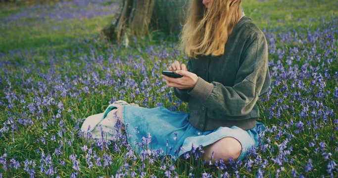 Young woman sitting in meadow with smartphone
