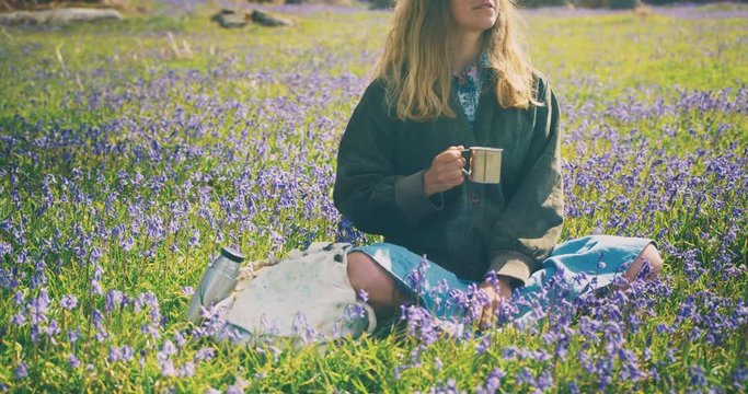 Young woman sitting in meadow drinking from cup
