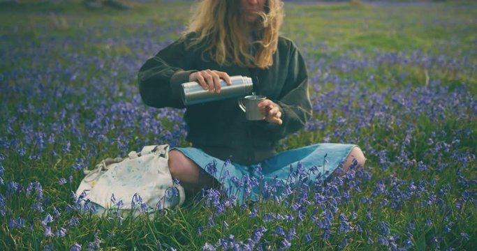 Young woman sitting in meadow pouring water from flask