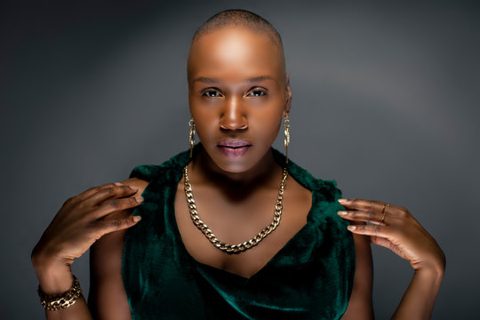 Beautiful black African American female model posing confidently with bald hairstyle in a studio.  The woman is wearing stylish fashion and portraying uniqueness and individuality.