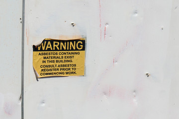 peeling black and yellow Asbestos Containing Materials Exist in this Building warning sign on the...