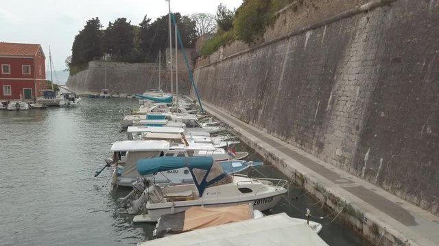 Slow tilt revealing small boats in a harbour and Ancient old city walls of Zadar, Croatia