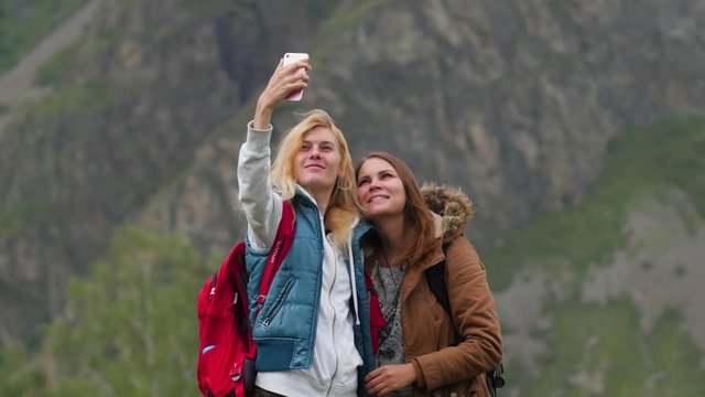 young women take pictures on the phone against the backdrop of the mountains. mobile communication in the mountains. communication concept. two girls do selfie on a background of mountains