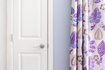 Home interior showing  colonial closet door with purple curtain decor and light blue painted wall.