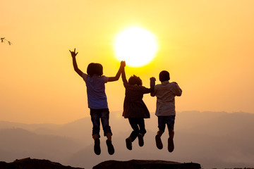 Silhouette of happy children jumping playing on mountain at sunset or sunrise time.