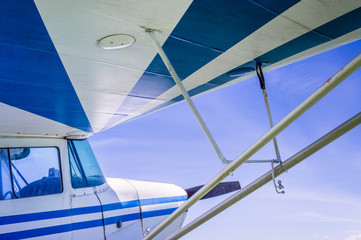 Underneath wing of blue and white striped small vintage aircraft with sunny blue sky.