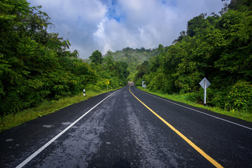 Fototapeta premium Asphalt road and mountains landscape under fog from rain with clouds