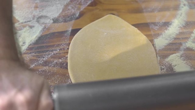 Male hands rolling round dough with roller pin for baking pie on wooden table. Chef hands rolling pizza dough with wooden roller. Baking pastry and cake in bakery. Cooking homemade food and pastry.