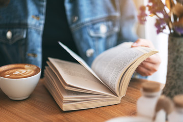 Closeup image of a woman holding and reading a vintage novel book while drinking coffee