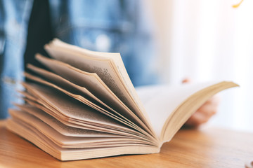 Closeup image of a woman holding and reading a vintage novel book on wooden table
