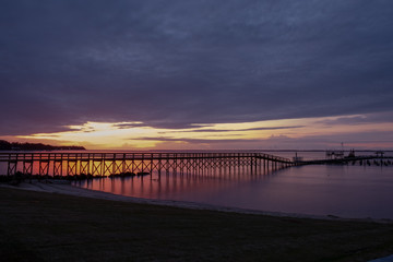 Obraz premium View from the shore of a long pier in front of a beautiful sunrise at the Neuse River estuary at a park in Minnesott Beach, North Carolina.