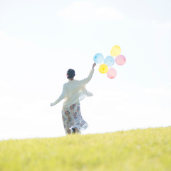 風船を持ち草原を走る女性の後姿