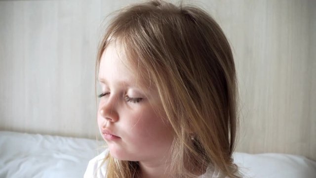 Blond girl wakes up in snow-white cravati. Little girl doesn't want to wake up