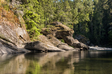 giant rock formation on the shore line of creek with forest behind on a sunny day