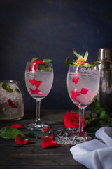 Sparkling cold water detox with rose and ice on the wood table there are rose, diferance glass, same object, cocktail shaker and ice placed around.