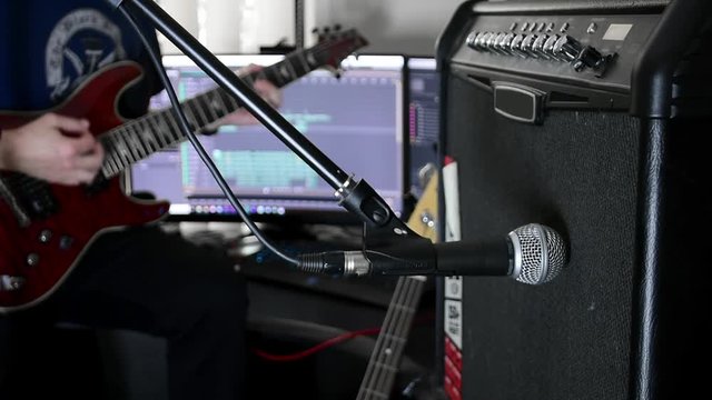 Musician playing a guitar with amp and microphone in foreground, recording on a computer