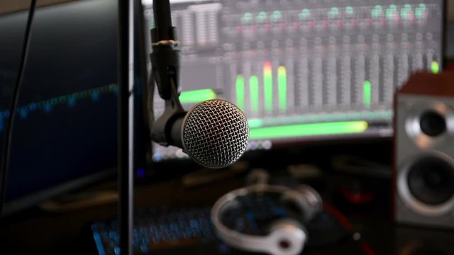 Locked-off shot of a microphone in close up, with computer monitors in the background