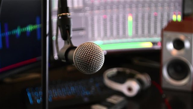 Smooth tracking shot of a microphone in close up, with computer monitors in the background