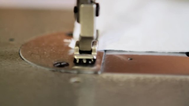 Tracking shot close up of a sewing machine operated by a tailor. Repairing a white piece of cloth.