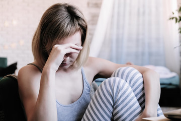 Beautiful blonde girl in pajamas is confused, upset and feeling unwell, sick at home, in pain.