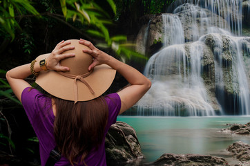 Young asia woman in hat with rucksack enjoying tropical waterfall in forest view in Thailand ,Travel and freedom concept.