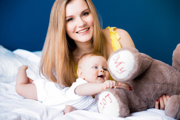 Smiling mom and infant girl kid playing with teddy bear in bedroom