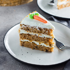 Slice of homemade carrot cake with cream cheese frosting on plate on gray stone table background