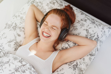 Obraz na płótnie Canvas Laughing woman with headphones in bed