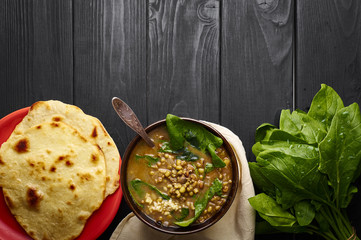 Mung Dhal with green Spinach and Chapati at black wooden tabletop. Moong Dal - Indian Cuisine curry. Vegetarian spicy dish.Top view Copy Space - obrazy, fototapety, plakaty