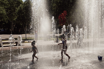 Silhouettes of children playing in spray fountains.