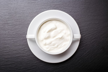 Greek yoghurt in white bowl on black slate background with copy space