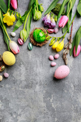 Colorful flowers and painted Easter eggs on grey, stone background