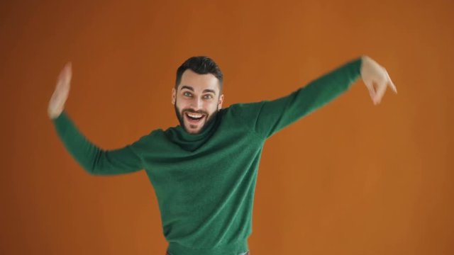 Portrait of joyful hipster dancing away making wave moves with arms on orange background. Playful silly millennials, happiness and positive emotions concept.