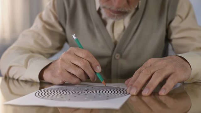 Concentrated retired man solving logic test at table, memory exercise, neurology