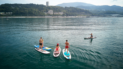 Aerial photography. The view from the top. A company of five young people in bathing suits doing yoga and photographed on SUP surfing in the black sea, Sochi. Active rest on the water.
