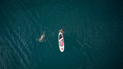 Aerial photography. The view from the top. Two girls in swimsuits swim in the open sea on SUP surfing. Doing yoga on the water.
