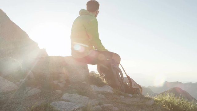 Panning shot of man sitting on top of mountain checking out the view of layered mountain peaks in the distance